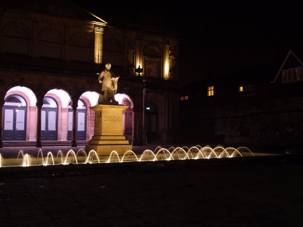 City square, with fountain and statue, floodlit